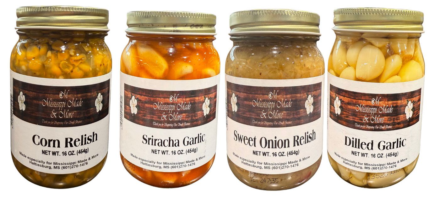 Four jars of pickled vegetables with gold lids on a white background, labeled corn relish, pickled garlic, and onions