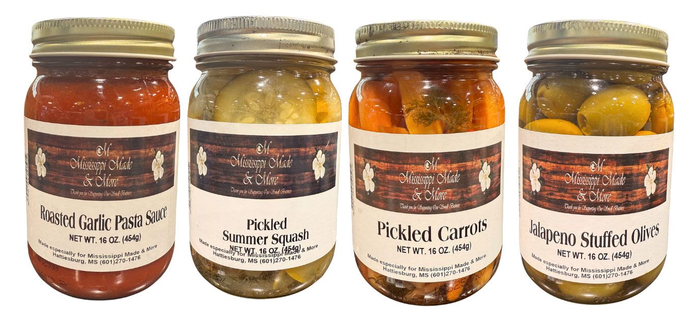 Four jars of assorted preserved condiments with gold lids and white labels displayed in a row