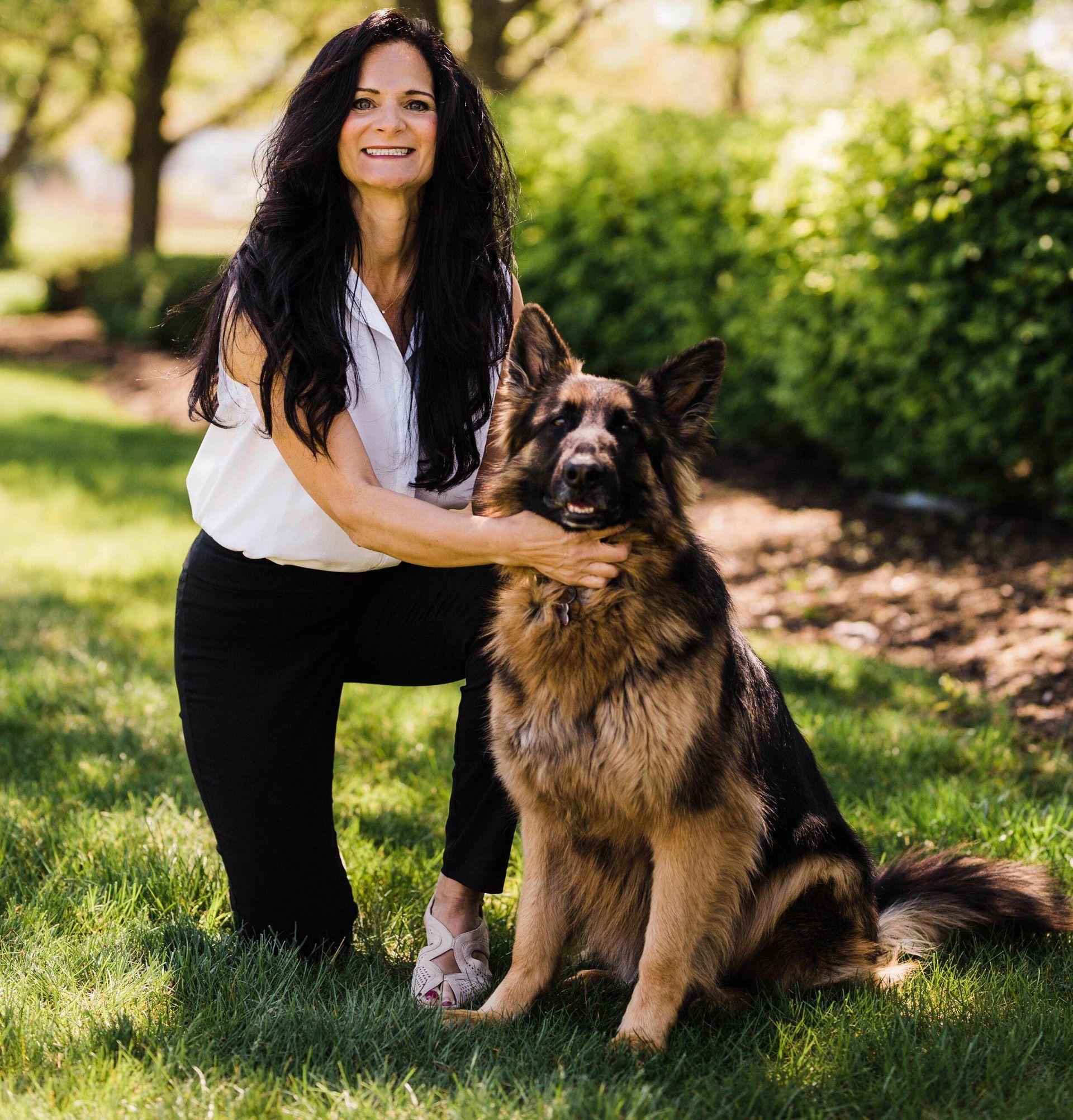 A woman is kneeling down next to a german shepherd dog in the grass.