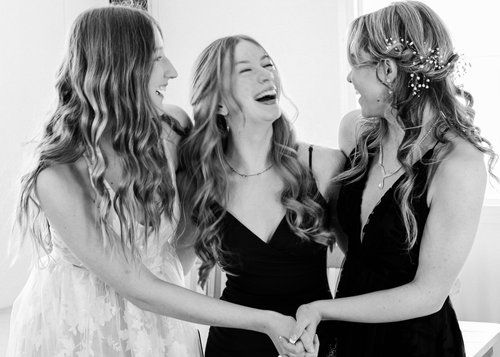 Three women are holding hands and laughing in a black and white photo.