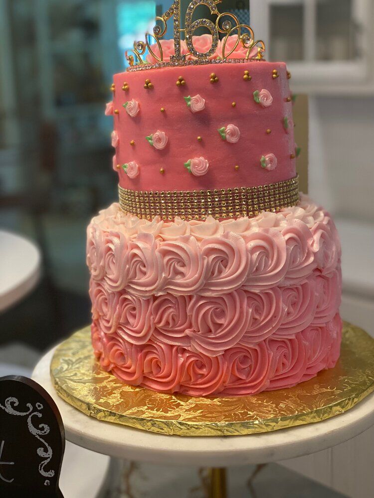 A pink and gold birthday cake with a tiara on top of it.