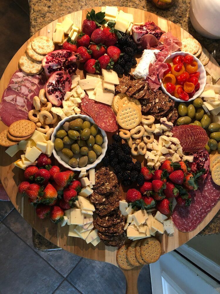 A wooden cutting board filled with meats , cheeses , crackers , strawberries and olives.