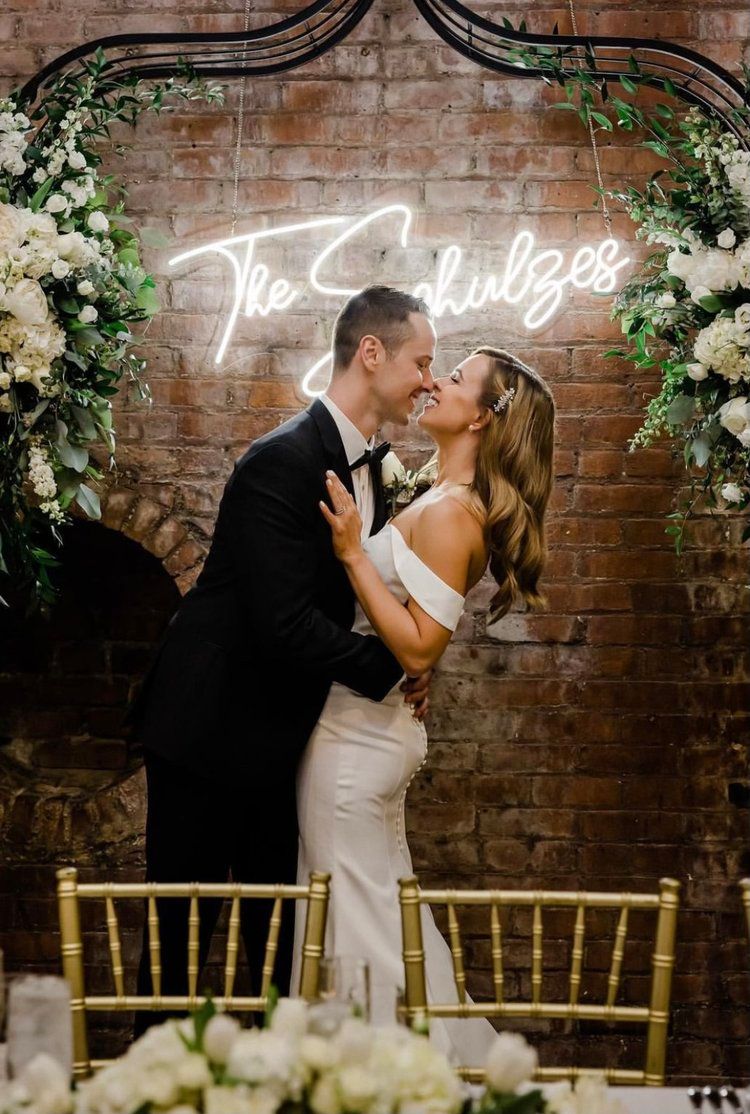 A bride and groom are kissing in front of a neon sign.
