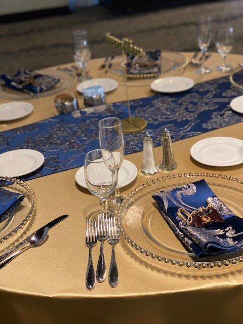 A table with plates , glasses , silverware and a blue table runner