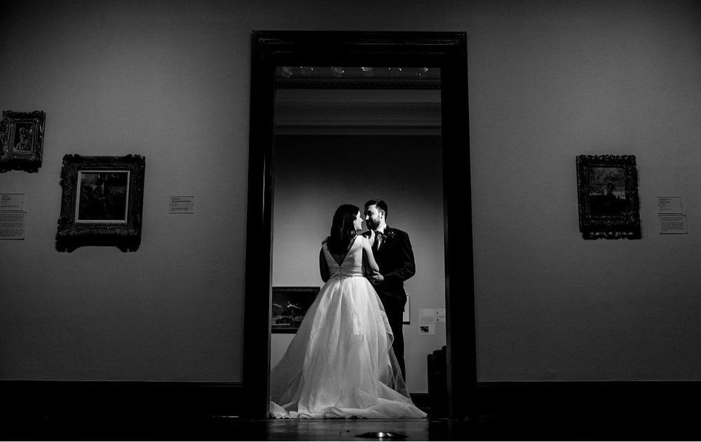 A bride and groom are kissing in a doorway in a museum.
