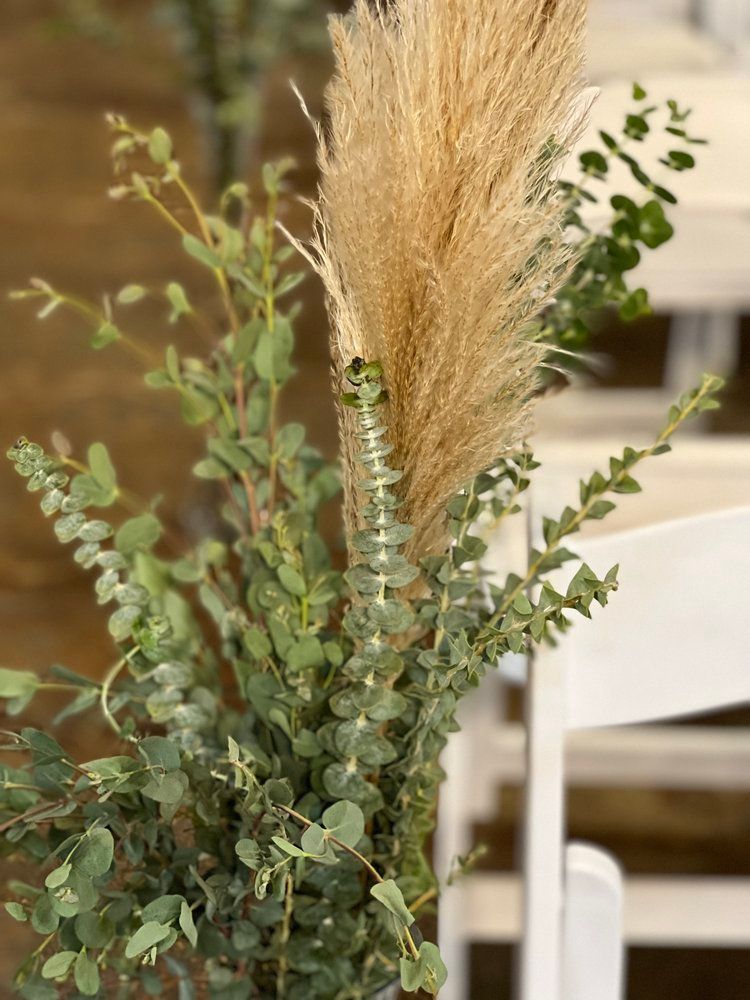 A vase filled with flowers and eucalyptus is sitting on a chair.