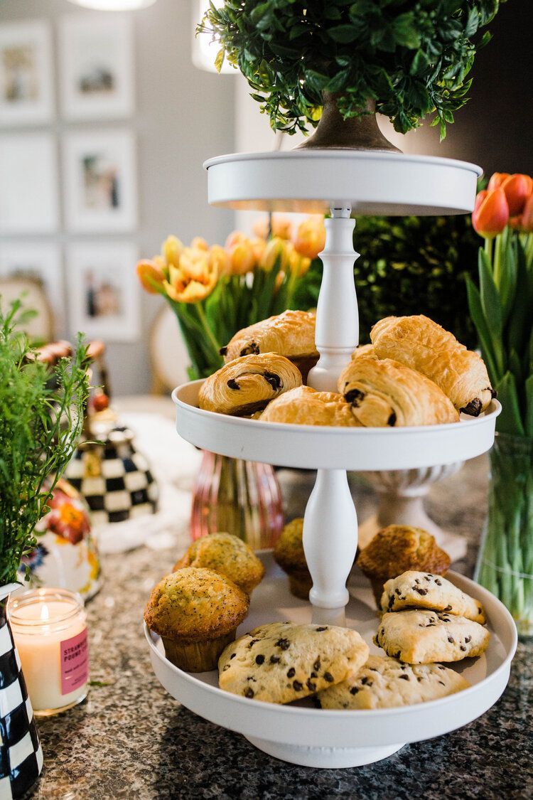A three tiered tray filled with muffins and cookies on a counter.
