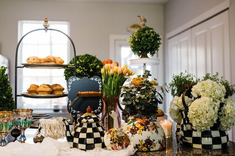 A kitchen counter filled with flowers , teapots , and muffins.