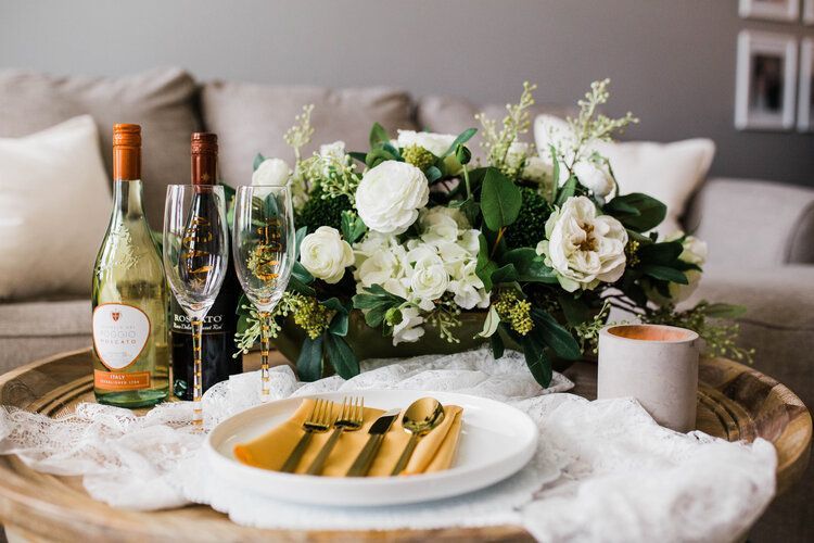 A table with a plate , utensils , wine bottles and flowers on it.