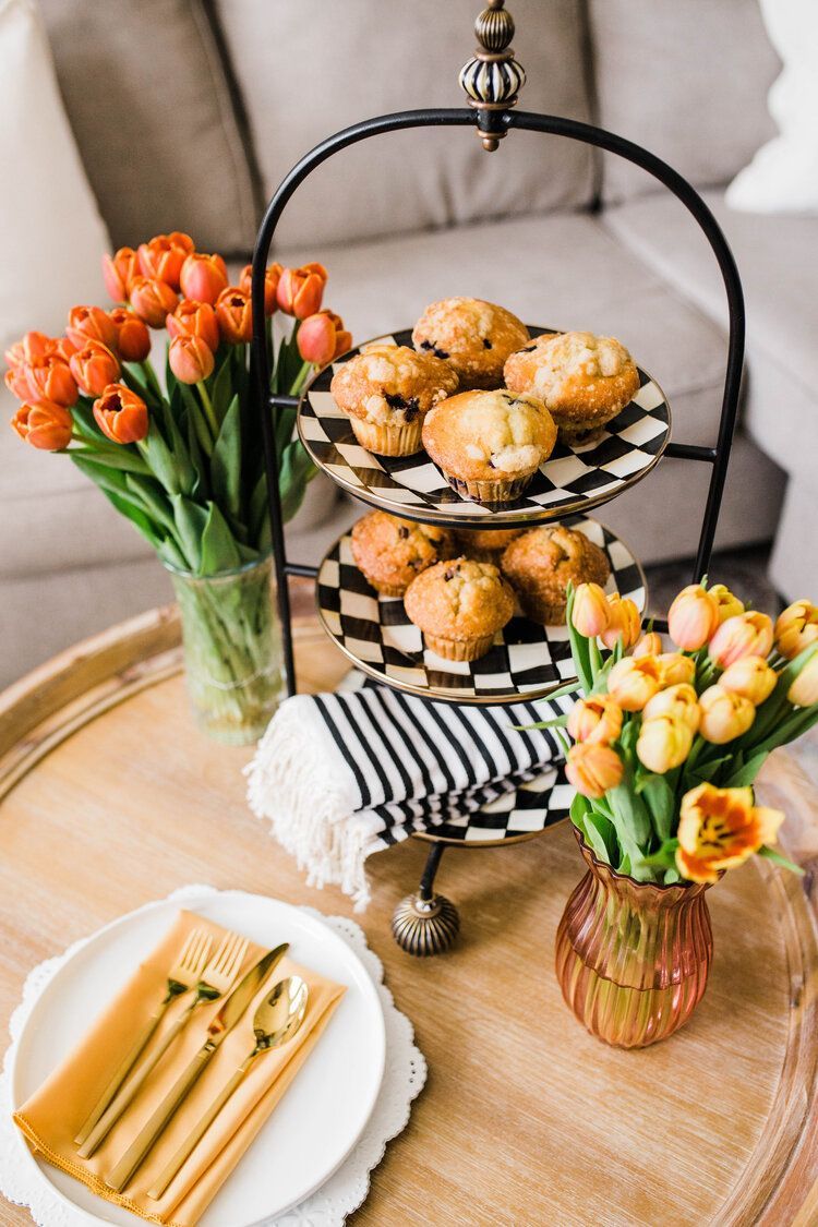 A table with three plates of muffins and flowers on it.