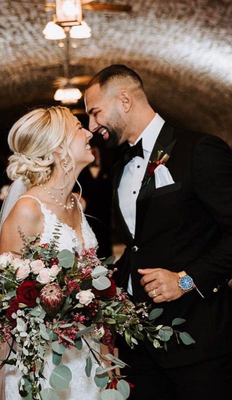 A bride and groom are looking into each other 's eyes while holding a bouquet of flowers.