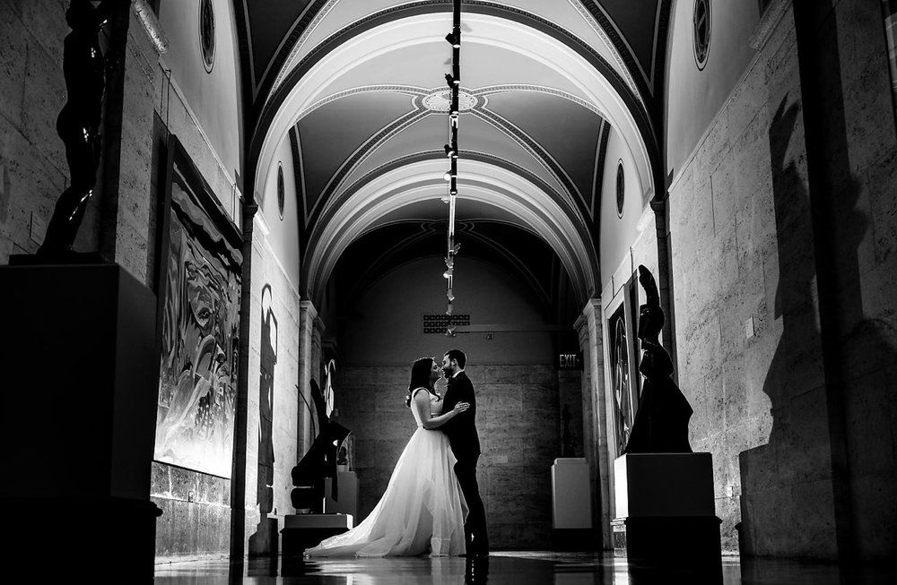 A bride and groom are kissing in a hallway of a museum.