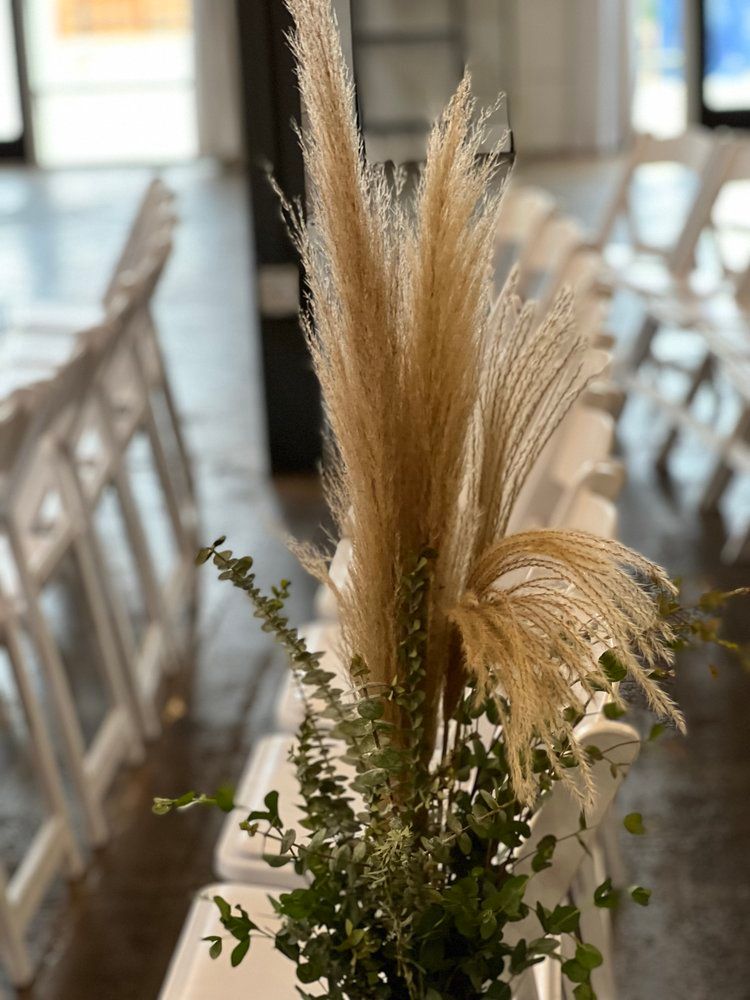 A vase filled with pampas grass and ferns is sitting on a table.
