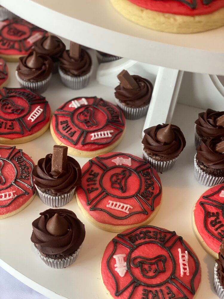 A table topped with cupcakes and cookies decorated to look like firefighters.