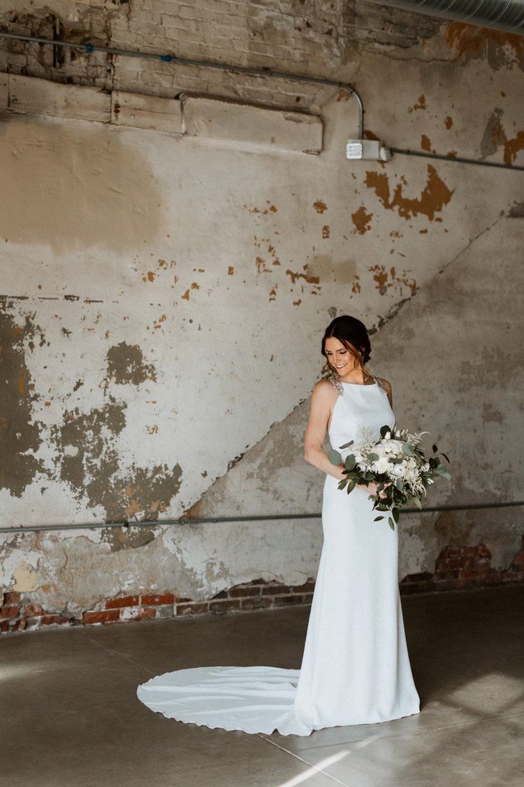 A woman in a wedding dress is standing in front of a wall holding a bouquet of flowers.
