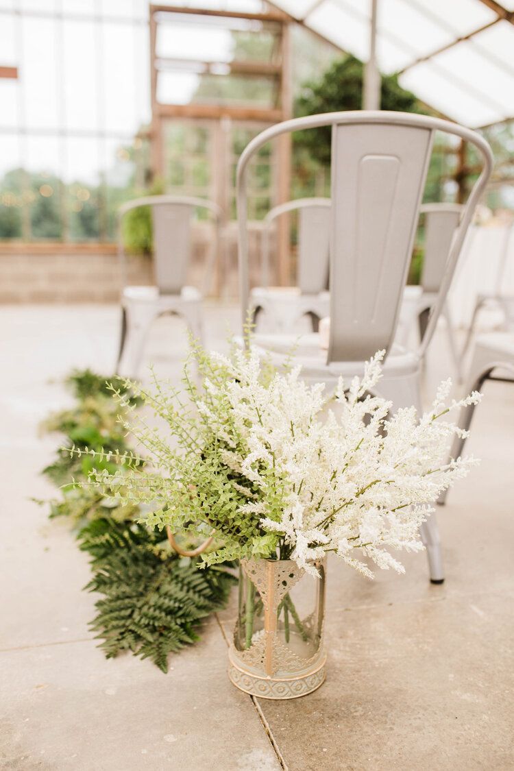 A vase filled with white flowers is sitting on the ground next to a row of chairs.