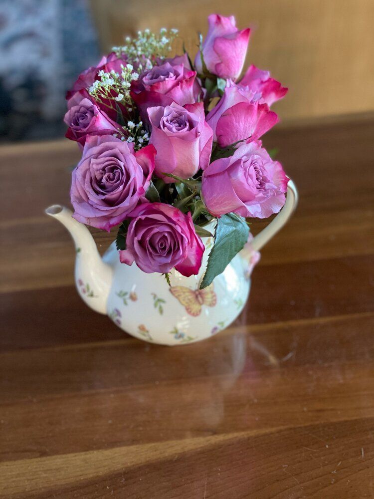 A teapot filled with pink roses is sitting on a wooden table.