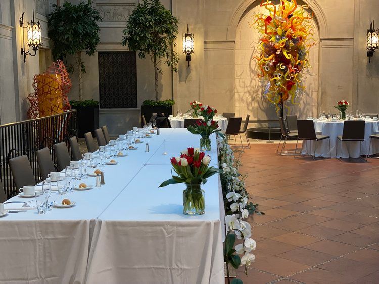 A long table with a vase of flowers on it in a room with tables and chairs.