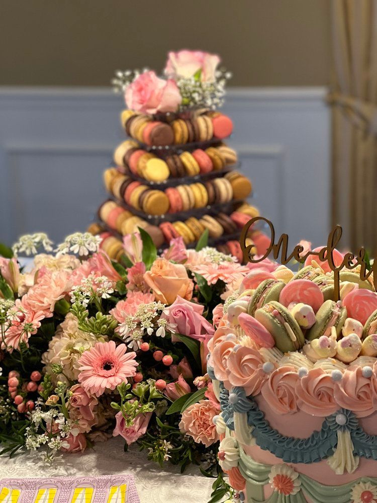 A cake with flowers and macarons on it is on a table.