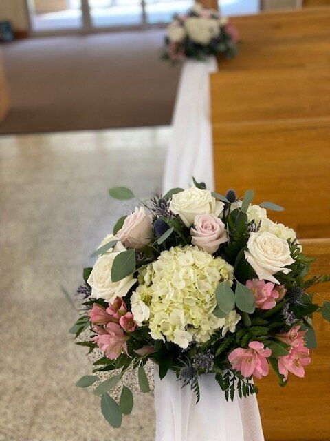 A bunch of flowers are sitting on a bench in a church.
