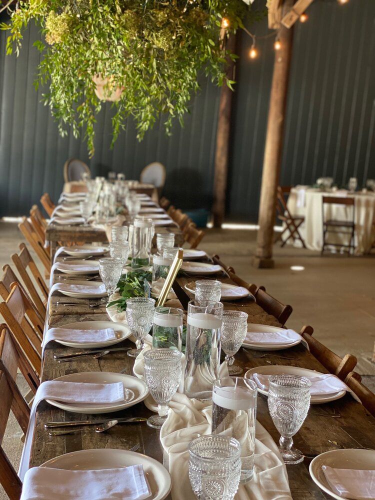 A long table with plates , glasses , and napkins set for a wedding reception.