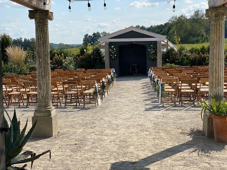 A row of wooden chairs are lined up in front of a building for a wedding ceremony.