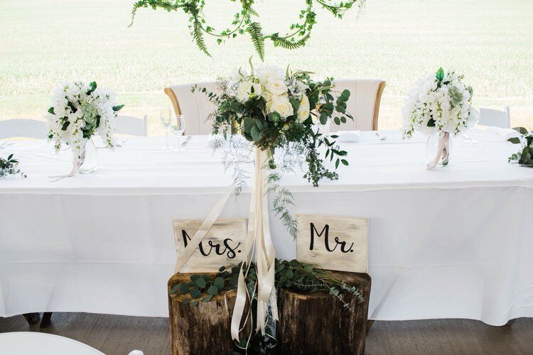The bride and groom 's table is decorated with flowers and wooden stump signs.
