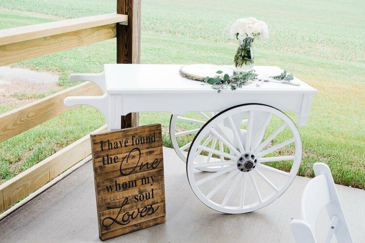 A white wagon with a sign on it is sitting next to a wooden fence.