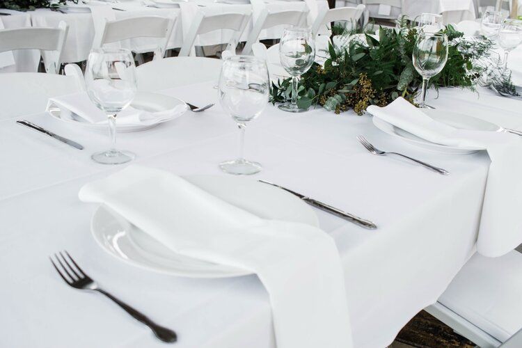 A table set for a wedding reception with white plates , silverware , and wine glasses.