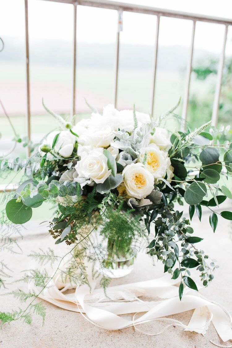 A vase filled with white flowers and greenery is sitting on a table.