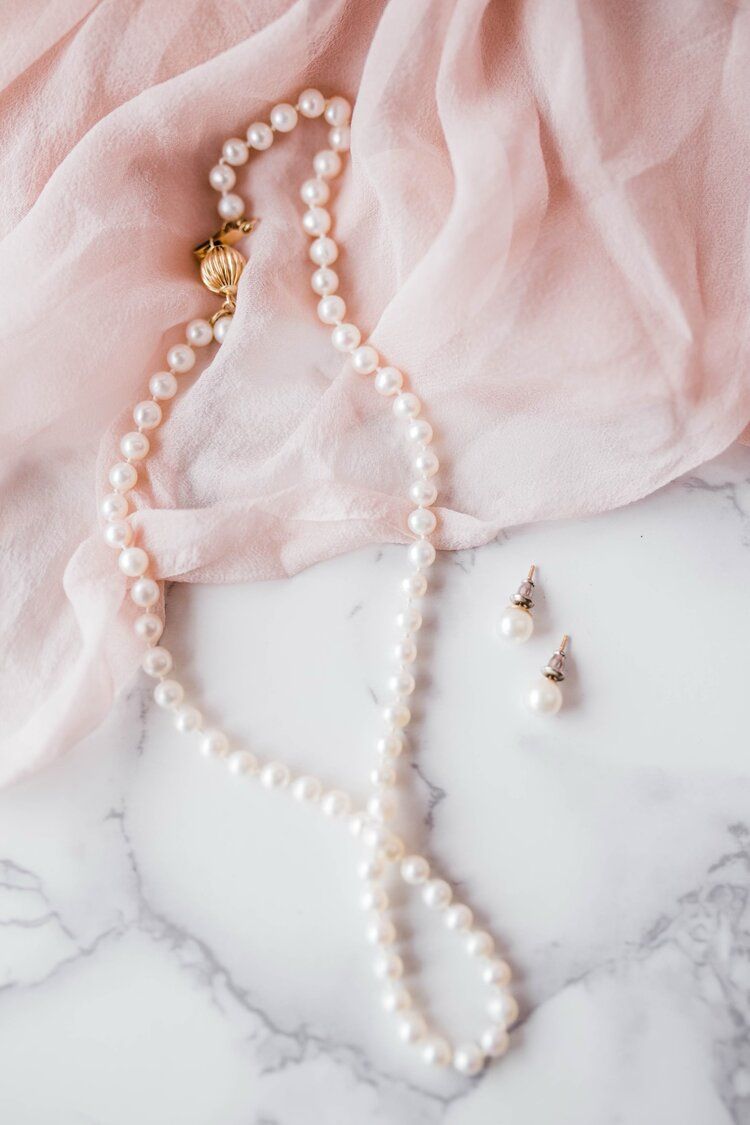 A pearl necklace and earrings are sitting on a marble surface.