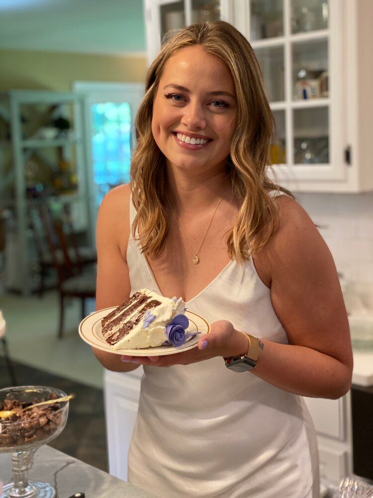 A woman in a white dress is holding a plate of cake.