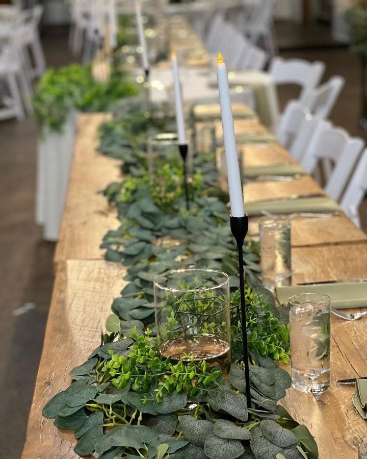 A long wooden table with candles and greenery on it.