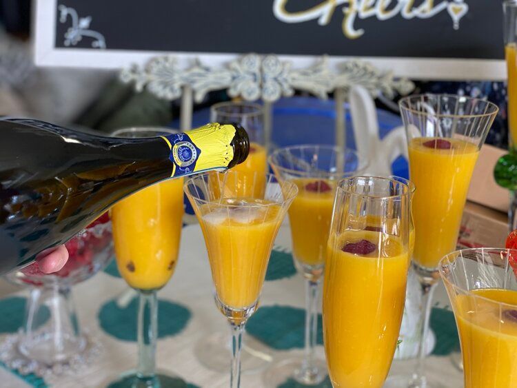 A bottle of champagne is being poured into a glass of orange juice.