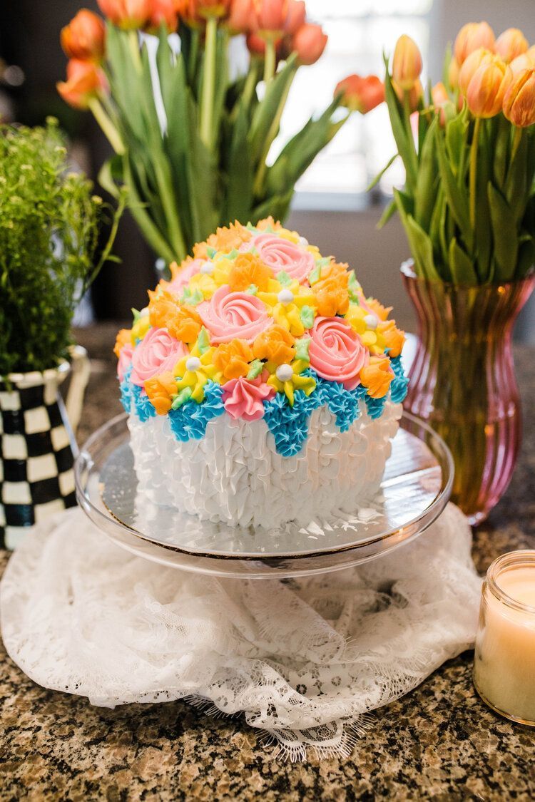 A cake with flowers on it is sitting on a glass plate on a counter.