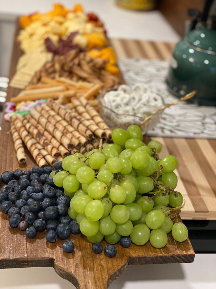 A wooden cutting board topped with grapes , blueberries , and wafer rolls.