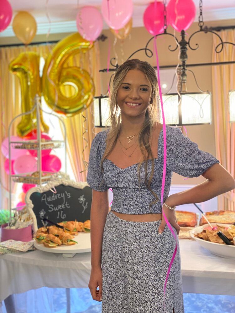 A woman is standing in front of a table with food and balloons.