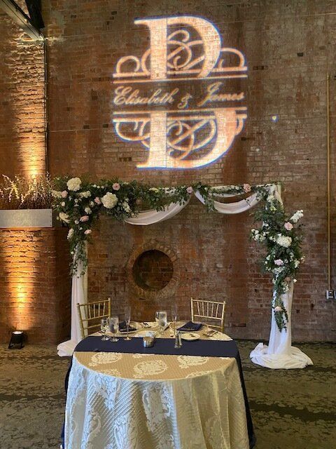 A table with a tablecloth and chairs in front of a brick wall.