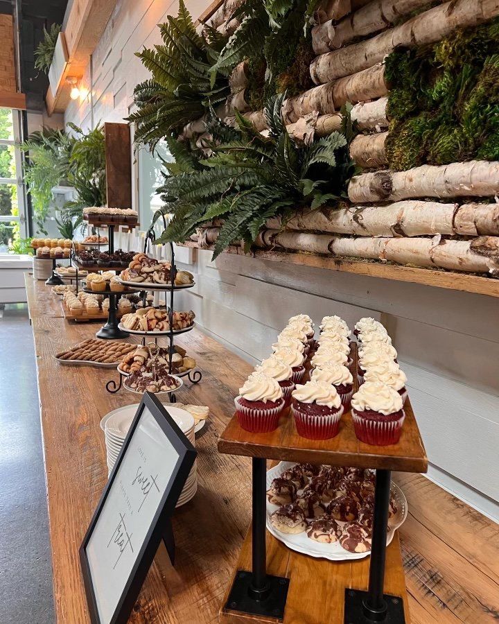 A long wooden table topped with cupcakes and a sign.