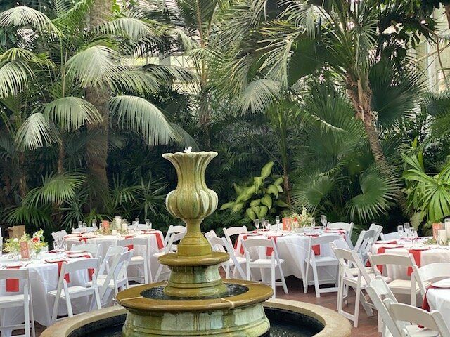 A fountain surrounded by tables and chairs with palm trees in the background