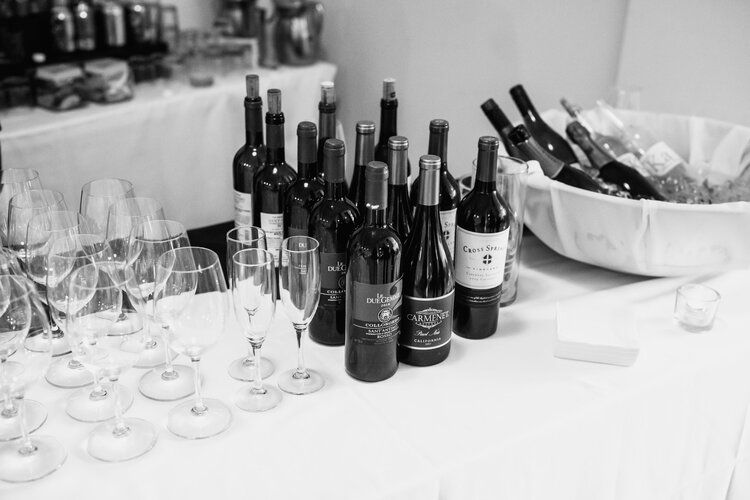 A black and white photo of wine bottles and glasses on a table.