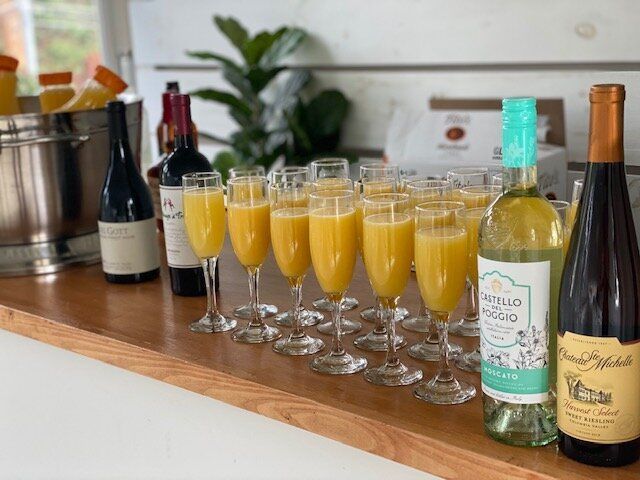 A row of glasses filled with orange juice and wine bottles on a counter.