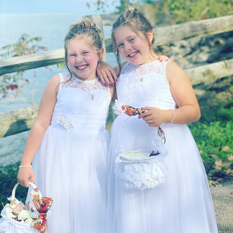 Two flower girls in white dresses are posing for a picture.