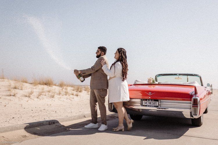 A man and a woman are standing next to a red convertible car.
