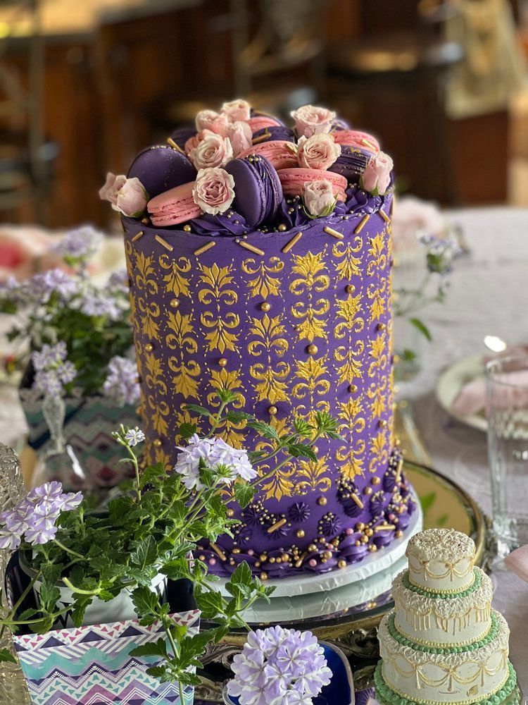 A purple and gold cake with flowers on top is sitting on a table.