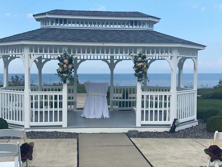 A white gazebo with a table and chairs in front of it overlooking the ocean.