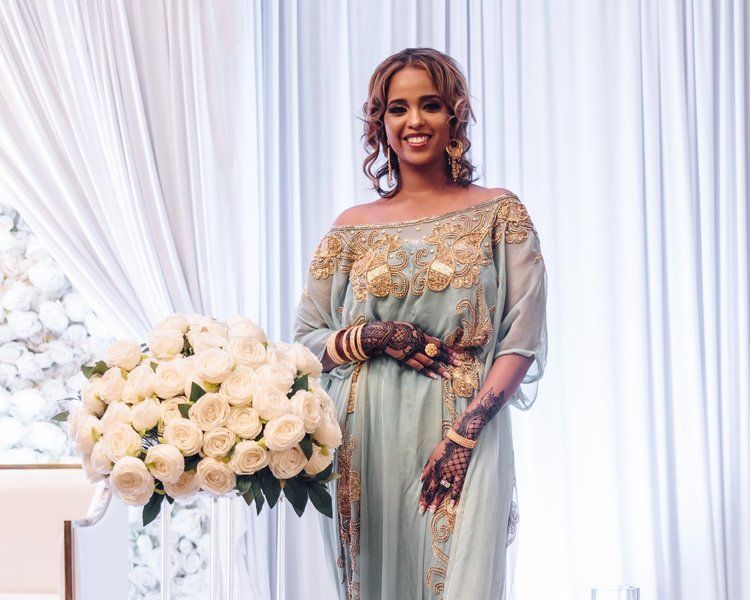 A woman in a blue dress is holding a bouquet of white roses.
