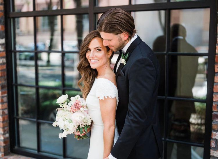 A bride and groom are posing for a picture in front of a window.