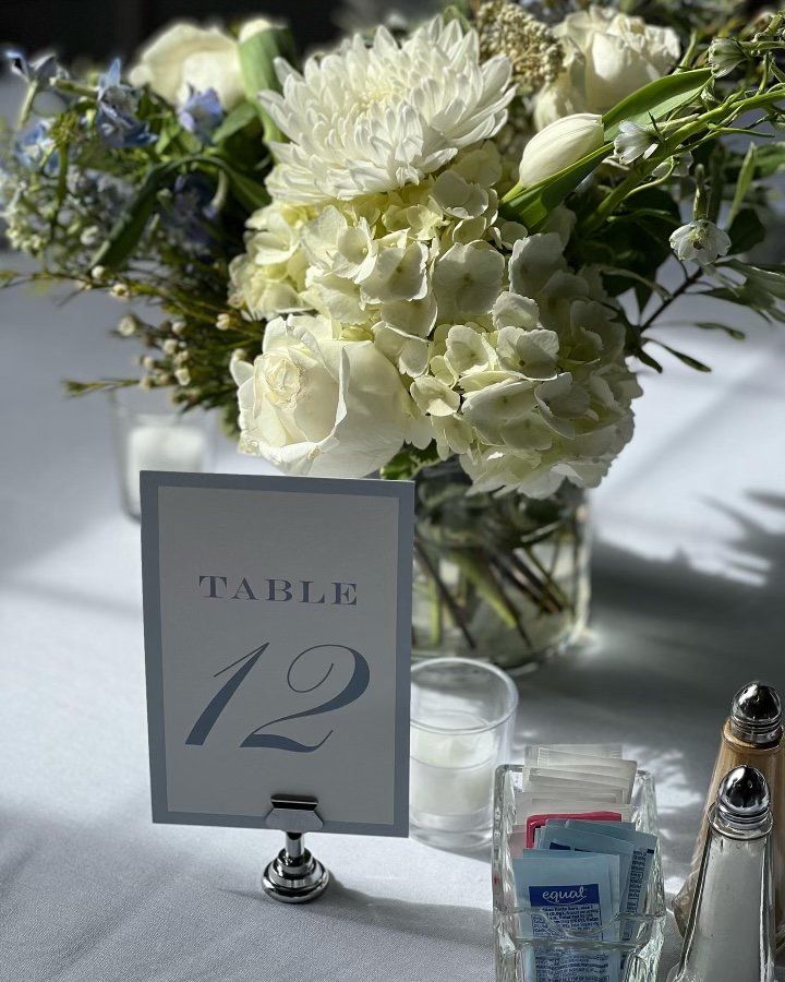 A table with a vase of white flowers and a table number 12