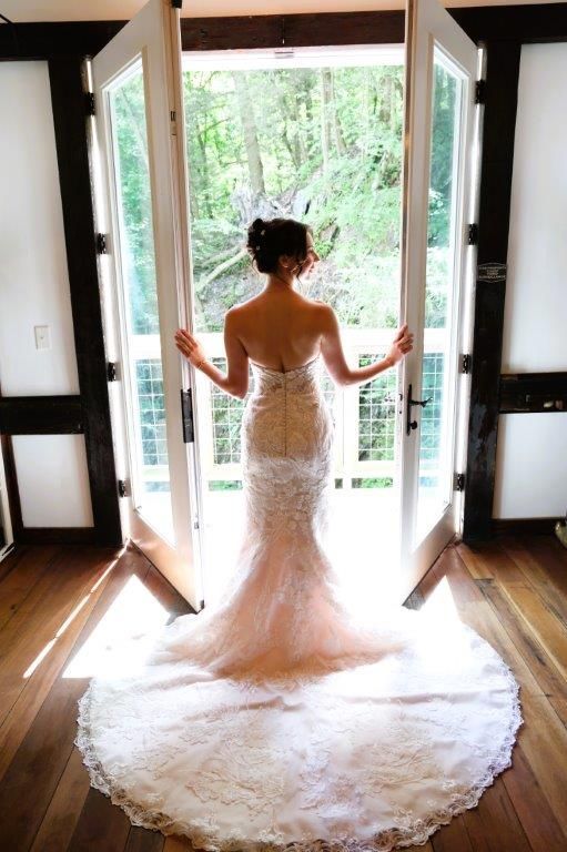 A woman in a wedding dress is standing in front of a window.